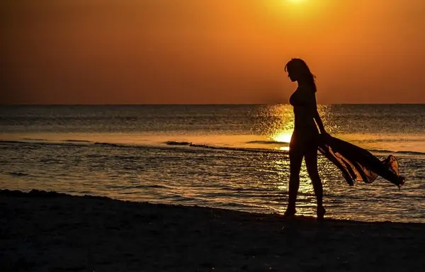 美しい少女が水面に沿って砂浜を歩いている 日没時に美しいセクシーな女の子のダークバックシルエット バックライト ナイスダークな背景 テキストの場所 — ストック写真