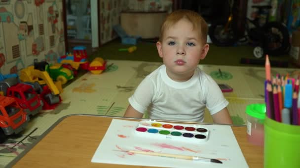 Niño Pequeño Sienta Una Mesa Con Pinturas Con Una Mirada — Vídeos de Stock