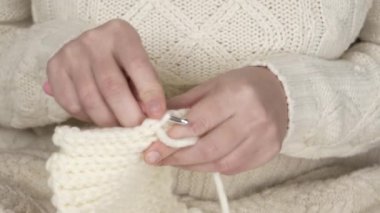 Tığ işi yakın plan. Kadınların elleri, kalın yün ipliklerle pembe örgü ören beyaz bir ürün örer. El sanatları, el sanatları, hobiler. Yüksek kalite 4k görüntü