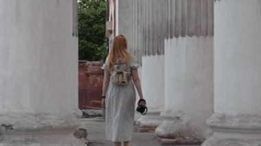 Elinde kamera olan kızıl saçlı bir kız kadim sütunlar boyunca yürüyor. Arkadan ateş ediyorlar. Bir turist eski bir binanın önünden geçiyor. Yüksek kalite 4k görüntü