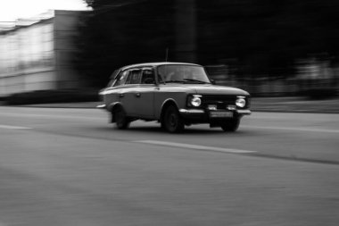 Bir retro araba yol boyunca sürüyor. Fotoğraf hareket halinde. Siyah beyaz fotoğraf. Arka plan bulanık. Yüksek kalite fotoğraf
