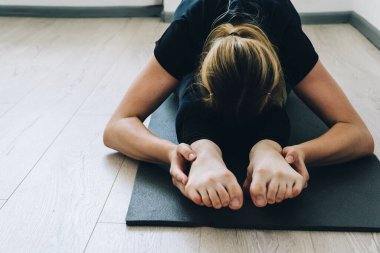 Genç esnek bir kız esneme hareketleri yapar ve spor minderinde yoga yapar. Yakın plan. Paschimottanasana pozu, eğitim. Stüdyoda jimnastik ve yoga dersleri var.
