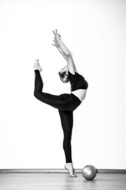 Esnek atletik kız jimnastikçi stüdyoda bir element sergiliyor. Beyaz arka planda ince bir balerin. Siyah beyaz fotoğraf.