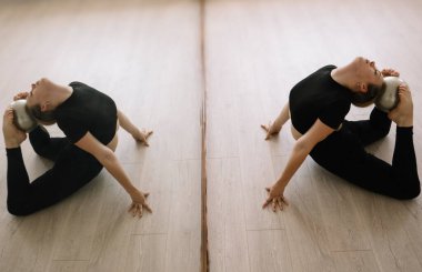 Siyah elbiseli genç bir atletik kız akrobatik hareketler sergiliyor. Aynadaki yansıma. Spor salonunda yoga ve jimnastik dersleri.