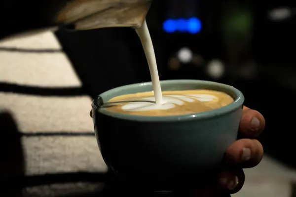Bir barista kahve köpüğünün üzerine bir tasarım çizer. Süt taze demlenmiş bir fincan kahveye dökülür. Yakın plan. Yüksek kalite fotoğraf