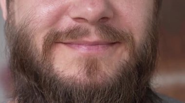 Uzun sakallı bir adam şüpheyle gülümsüyor. Bir erkeğin aşırı yakın plan gülümsemesi. Ağır çekim. Yüksek kalite 4k görüntü