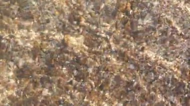 Güneşli bir günde kristal berrak deniz suyu. Kumlu deniz dibi, su altında. Dalgalanma ve dalgalar parlak güneş ışığını yansıtıyor. Kapatın. Yüksek kalite 4k görüntü