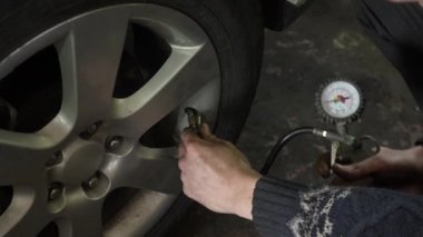 Bir arabanın lastiklerini değiştirmek. Bir adam sıkıştırılmış havayla lastikleri şişirir ve basınç göstergesine bakar. Otomobil tamircisi elleri yakın çekim. Yüksek kalite 4k görüntü