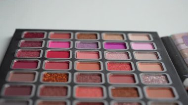 Beyaz arka planda izole edilmiş çok renkli göz gölgelerinin renkli paleti. Gölgelerin parlak ve değişik tonlarında, mat ve parlak. Profesyonel göz estetiği. Kablolar yakın çekim. Ağır çekim. 4k 