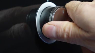 Fırının ısı kontrol düğmesini ayarlayan bir elin yakın çekimi, pişirme sıcaklığını düzenleme sürecini gösteriyor. Resim mutfak aletleriyle olan dokunsal etkileşimi vurgular