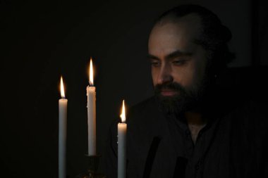 Sakin bir ifadeyle loş bir odada mumlara bakarak düşünceli ve huzurlu bir atmosfer yaratıyor. Sahne, sessiz bir yansımayı yakalar. Yüksek kalite fotoğraf