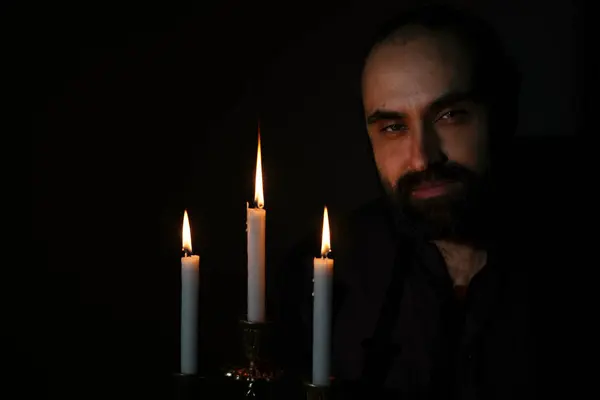 Dalgın bir ifadeye sahip bir adam loş ışıkta oturur, üç mumla aydınlatılır. Huzurlu ortam ve nazik mum ışığı onun iç gözlem ruh halini vurguluyor..