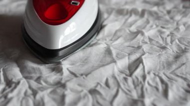  Beyaz kumaş bir yüzey üzerinde süzülen modern buhar ütüsünün yakın plan görüntüsü, parlak tasarımı ve işlevselliğini vurguluyor. Ütünün ön kısmına odaklan. Yüksek kaliteli FullHD görüntüler