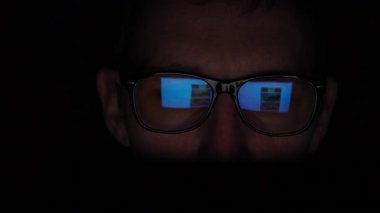 Akşamları ekranın önünde oturan bir adamın yakın çekimi. Hızlı haber yayını gözlüklerine yansıyor. Loş ışık dramatik ve yoğun bir hava yaratır. Yüksek kalite 4k görüntü
