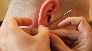 Steril iğneyle bir adamın kulağını delen profesyonel bir piercingçinin yakın çekimi. Müşterilerin kulakları hassasiyet için nazikçe tutulur. Sahne hijyenik koşulları ve titiz tekniği gösteriyor. 4k