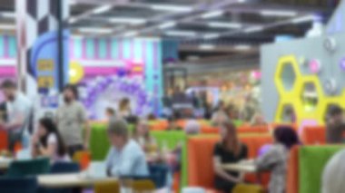 Parlak, modern bir yemek salonunda yemek yiyen ve sosyalleşen insanların bulanık görüntüsü. Sahne renkli mobilyalar, canlı bir iç tasarım ve rahat bir atmosfer içeriyor. Bulanık görüntüler 