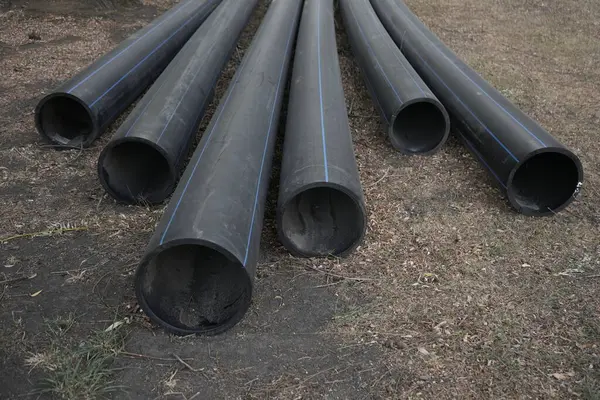 Büyük siyah plastik borular dışarıda yerde yatıyor. Görüşün sonu. Lağım boruları, su boruları, ısıtma boruları.