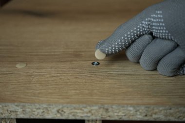 Eldivenli el, kapak kapağını kaplamalı çipin içine yerleştiriyor. Mobilya montaj süreci, yakın çekim görüntü... yüksek kalite fotoğraf