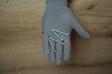 Gri koruyucu eldiven, mobilya veya ahşap eşya montajı için birkaç metal vida tutuyor..