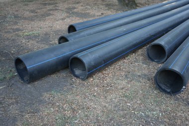 Açık arazide yatan siyah polietilen borular tesisat ya da altyapı kurulumuna hazır..