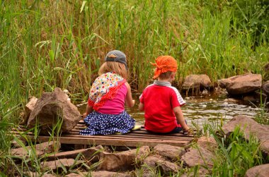 İki çocuk dere kenarındaki küçük tahta bir köprüde oturuyordu. Etrafı uzun otlar ve taşlarla çevriliydi. Açık hava çocukluğu, doğa keşfi ve aile macerası..