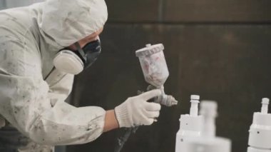 A worker in a mask and uniform paints a metal pipe at the factory, with paint under pressure. High quality 4k footage