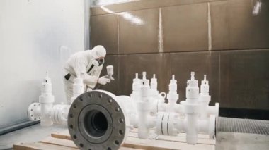 A worker in a mask and uniform paints a metal pipe at the factory, with paint under pressure. High quality 4k footage