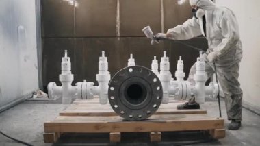 A worker in a mask and uniform paints a metal pipe at the factory, with paint under pressure. High quality 4k footage