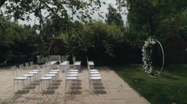 Şeffaf ağırlıksız sandalyeler. Gelin ve damadın ruhsatı için yuvarlak çiçek kemeri. Düğün yeri yaz ya da ilkbaharda. Yoğun yeşil bitki örtüsü. Modern düğün dekoru. Yüksek kalite 4k görüntü