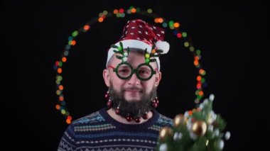 Noel Baba şapkalı genç bir adam sakalında oyuncaklarla arka planda yeni yıl ışıkları ve boynuz şeklinde yeni yıl gözlükleriyle. Elinde bir ağaç tutarak Mary Christmas diye bağırır..