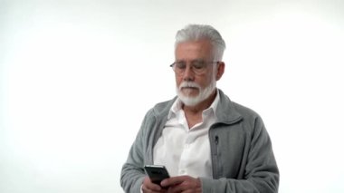 Yaşlı, sakallı, stil sahibi bir adam telefona hüzünle ve hayal kırıklığıyla bakar. Akıllı telefonu olan bir emekli, konsept. Yüksek kaliteli FullHD görüntüler