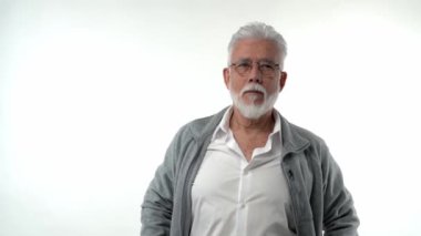 Emekli bir adamın portresi ciddi bir yüz ifadesiyle duruyor, deneyimlere odaklanmış bir şekilde düşünüyor. Beyaz bir arka planda. Ellerini cebine koy, önüne bak. 