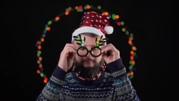 Junger Kerl Mit Nikolausmütze Spielzeug Auf Dem Bart Und Silvesterbeleuchtung — Stockvideo
