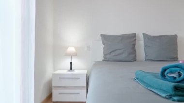 Rahatlamak ve havlunun üzerinde şekerle uyumak için modern minimalist yatak odası. Gri yastıklar için komodinlerin üzerinde minimalist lamba. Yüksek kalite 4k görüntü