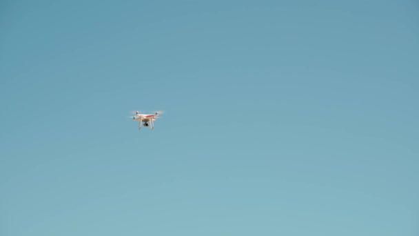 背景に青空を背景に空中に浮かぶ高解像度ビデオカメラを搭載したホワイトリモートコントロールドローン 高品質4K映像 — ストック動画