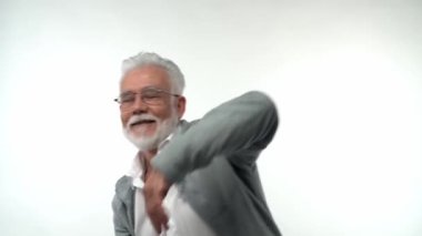 Gözlüklü ve sakallı emekli yaşlı bir adam neşeyle dans ediyor, elleriyle el kol hareketi yapıyor. Mutlu yaşlılık konsepti. Yüksek kaliteli FullHD görüntüler