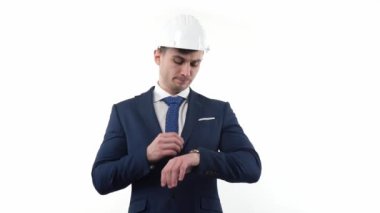 A young businessman in a suit and helmet looks at his watch in anticipation of events. The concept of ponctuality and discipline. High quality FullHD footage
