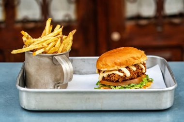 Classic fried chicken burger with vegetables and fried potatoes in a vintage mug and metal tray. High quality photo
