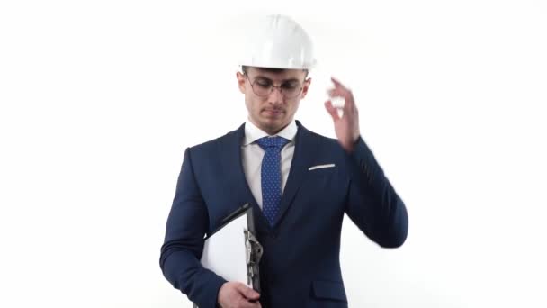 問題を解決することを考えて 白い背景に保護ヘルメットの眼鏡をかけたスーツの男ビジネスマンは 彼の手にメモ帳を保持します — ストック動画