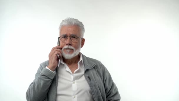 白い背景の携帯電話で話してメガネを引退した男性の肖像画 独立したスタジオを背景に髭を生やした白髪の祖父 スローモーション 高品質 — ストック動画
