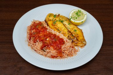 Fresh fried fish fillet garnished with rice in tomato sauce and herbs. High quality photo