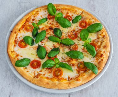 Caprese pizza with suluguni cheese and tomatoes, covered with pesto sauce. On a wooden background in a plate. High quality photo
