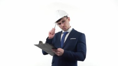 Koruyucu kask takan takım elbiseli bir erkek işadamı not defterindeki bir kalemle plan yapar ve düşünür. Beyaz bir arkaplanda
