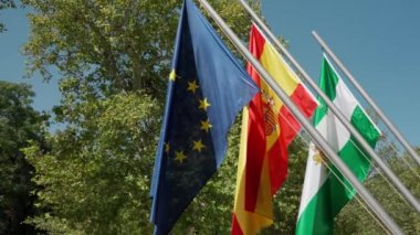 EU, Spain and Andalusia flag waving in slow motion against green trees and blue sky. High quality 4k footage