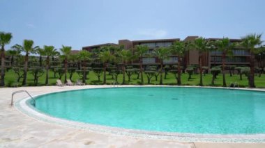 A beautiful hotel for relaxation with a swimming pool with railings and blue water. Lawn with palm trees. High quality 4k footage