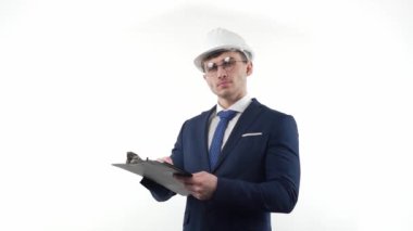Male businessman in a suit with glasses in a protective helmet thinks and makes planning notes with a pen in a notebook. On a white background. High quality FullHD footage