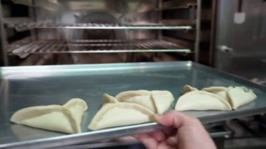 A bakers hand inserts a tray of raw empanadas into an industrial oven. High quality 4k footage