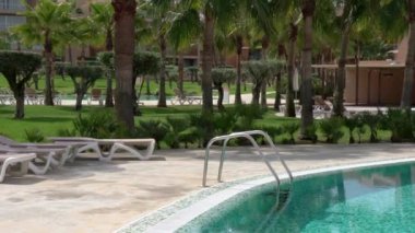 Rahatlamak için güzel bir otel. Parmaklıkları ve mavi suyu olan bir yüzme havuzu. Palmiye ağaçları ile çim. Dinlenmek için güneşlik. Yüksek kalite 4k görüntü