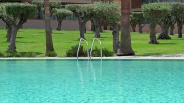 A beautiful hotel for relaxation with a pool with railings and blue turquoise water. Lawn with palm trees. High quality 4k footage