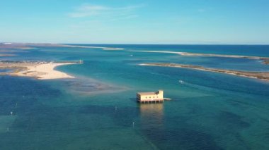 Hava görüntüsü. Fuseta köyü üzerinde Ria formosa adlı doğal Portekiz parkı üzerinde insansız hava aracı uçuşu. Körfezin ortasında turkuaz suyu olan bir kurtarma evi..